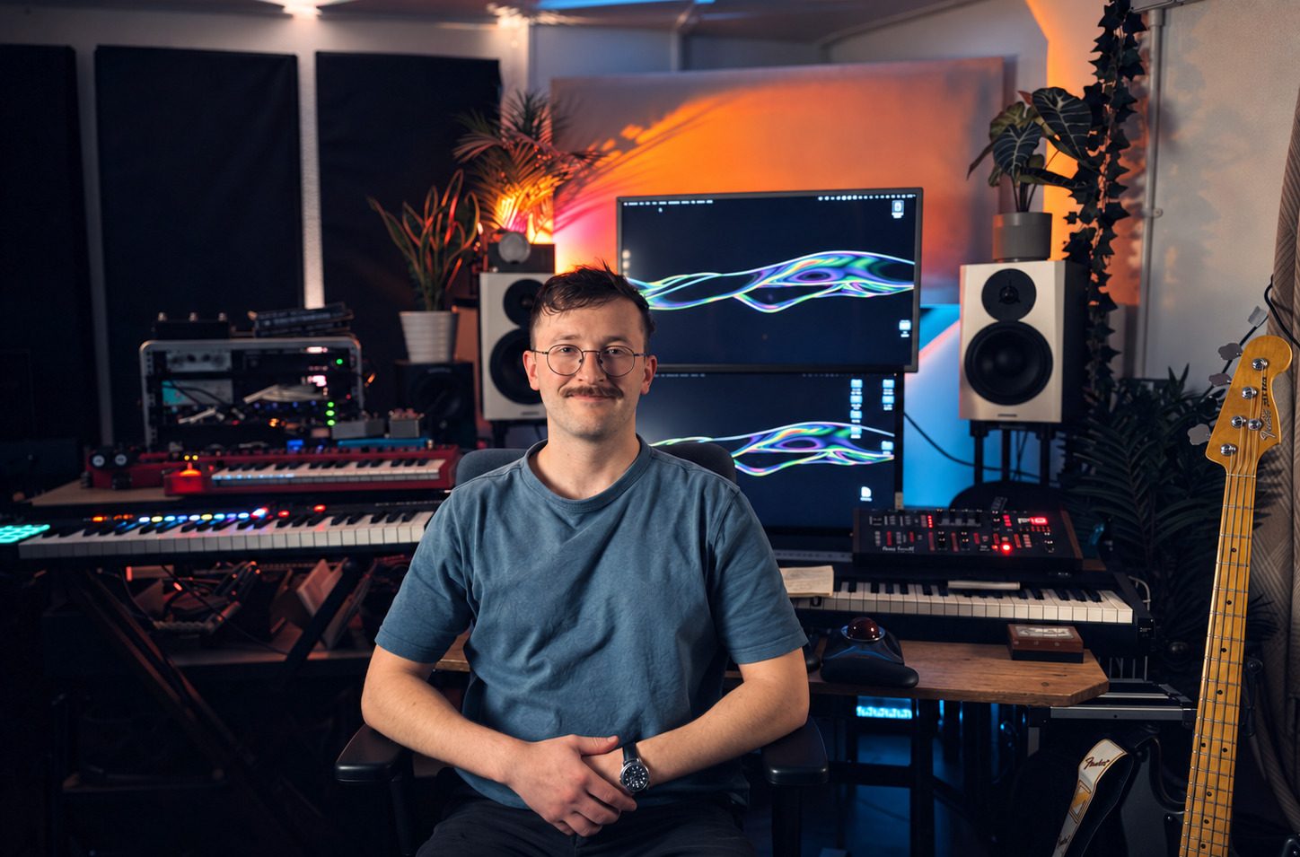 Max Greaves sitting at his studio desk facing the camera, with studio monitors, screens, a MIDI keyboard and outboard rack behind him.