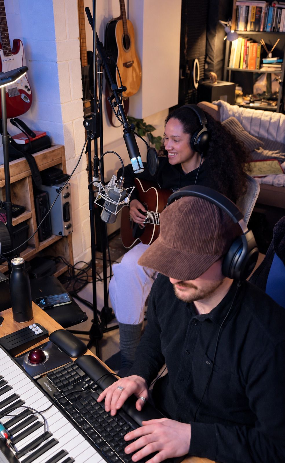 Max Greaves at the keyboard while an artist records a vocal at the microphone behind him, both in headphones.
