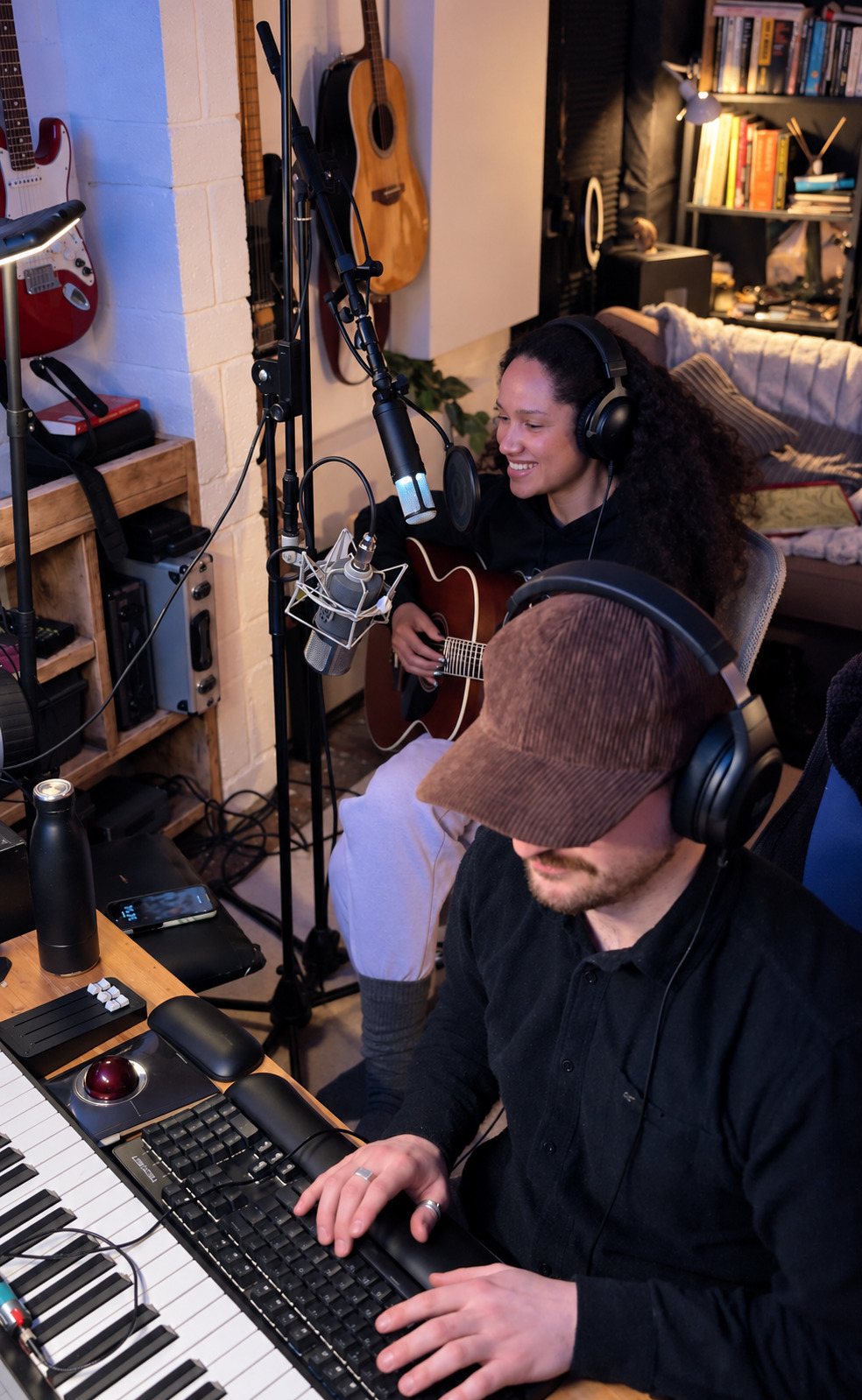 Max Greaves at the keyboard while an artist records a vocal at the microphone behind him, both in headphones.